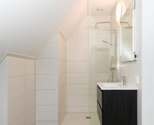 seitenansicht des badezimmers mit rundem angenemen lampe dunkle bodenfließen und helle wandfließen sowie einen quadratischen spiegel mit seitenlicht