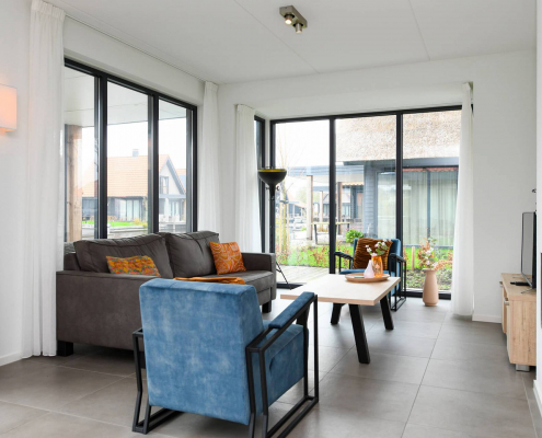 Wohnzimmer mit grauem sofa orangenen kissen und blauen sesseln sowie eine schöne sicht nach drausen
